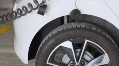 Kadın bir arabanın önünü açıyor ve elektrik kablosunu kamu şarj noktasında şarj olduktan sonra elektrikli araçtan çıkarıyor..