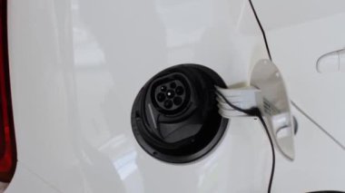 Bir kadın halka açık şarj istasyonundaki araba prizine bir fiş takıyor. Elektrikli araç aküsü şarj oluyor.