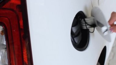Kadın elektrikli beyaz bir arabanın şarj prizini bağlıyor. Çevre dostu ve sıfır emisyonlu araba.