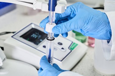 Lastik eldivenli bir kadın pH metre kullanarak çözeltinin pH 'ını ölçmek için cam elektrot tutuyor. Analitik veya elektro kimya laboratuvarı. 