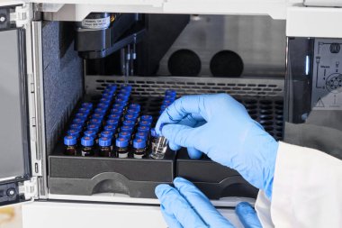 Kadın eli kapalı lastik eldiven ile cam bir şişe içine numune koyun mavi kapaklı HPLC sistemindeki otomatik ampler rafına. Ayrıştırma bileşikleri için yüksek performanslı sıvı kromatografi. Bilimsel