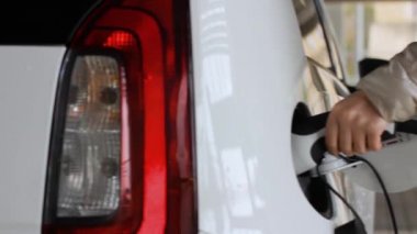 Kadın, halka açık noktadan şarj ettiği için elektrikli araba EV 'sinin fişini çekiyor.