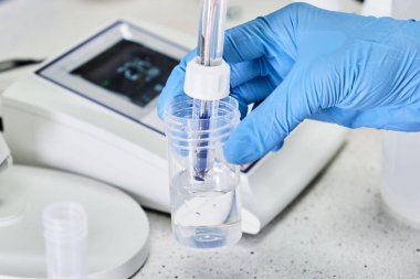 Lastik eldivenli bir kadın pH metre kullanarak çözeltinin pH 'ını ölçmek için cam elektrot tutuyor. Analitik veya elektro kimya laboratuvarı. 