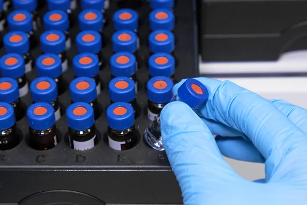 Nahaufnahme Frau Hand in einem Gummihandschuh legen Probe in einem Glasfläschchen mit blauer Kappe in die Autosampler-Rack in HPLC-System. Hochleistungs-Flüssigchromatographie für Trennmittel. Wissenschaftliche — Stockfoto