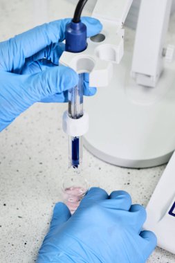 Lastik eldivenli bir kadın pH metre kullanarak çözeltinin pH 'ını ölçmek için cam elektrot tutuyor. Analitik veya elektro kimya laboratuvarı. 