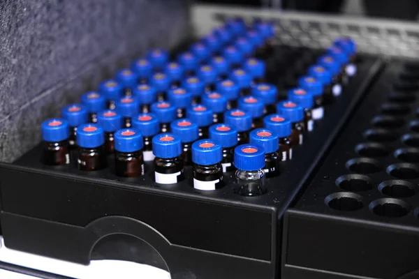 Glasflaschen mit blauen Kappen befinden sich im Rack des HPLC-Systems mit Autosampler. Trennung von Verbindungen in chemischen oder klinischen Labors. Wissenschaftliche und Forschungsarbeiten. Entwicklung von Arzneimitteln. — Stockfoto