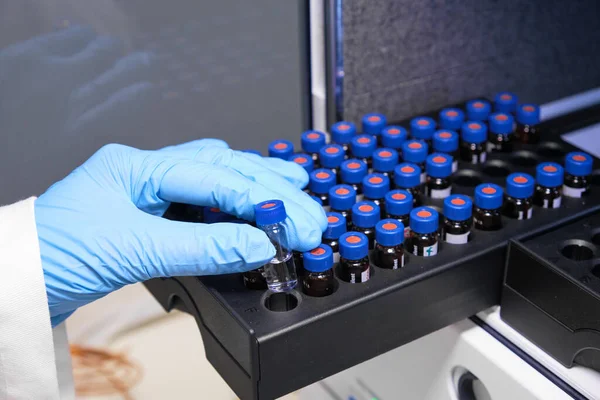 Nahaufnahme Frau Hand in einem Gummihandschuh legen Probe in einem Glasfläschchen mit blauer Kappe in die Autosampler-Rack in HPLC-System. Hochleistungs-Flüssigchromatographie für Trennmittel. Wissenschaftliche — Stockfoto