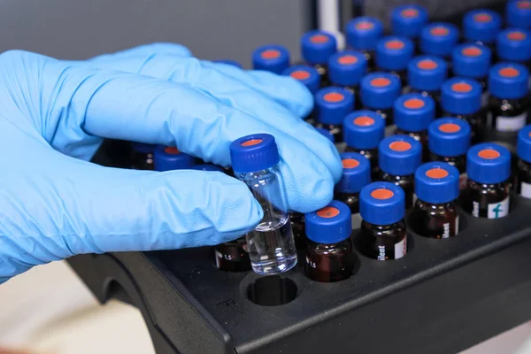 Close up woman hand in a rubber gloves put sample in a glass vial with blue cap into the autosampler rack in HPLC system. High performance liquid chromatography for separation compounds . Scientific — Stock Photo, Image