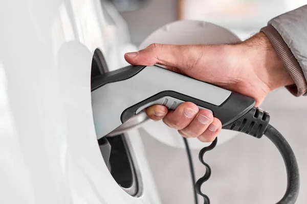 Primer plano mans mano sosteniendo carga de coche eléctrico conectado a coche eléctrico en la estación de carga pública. Vehículo respetuoso del medio ambiente y cero emisiones . — Foto de Stock