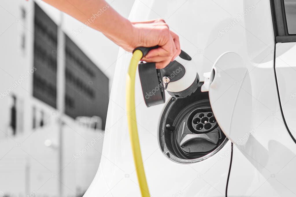 Electric car power supply charging on charger. Closeup up woman hand inserting a charger plug to electric vehicle. 