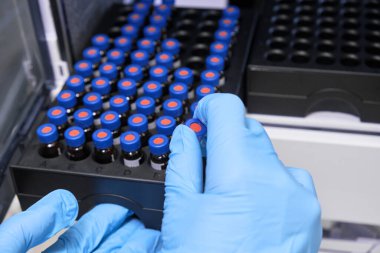Kadın eli kapalı lastik eldiven ile cam bir şişe içine numune koyun mavi kapaklı HPLC sistemindeki otomatik ampler rafına. Ayrıştırma bileşikleri için yüksek performanslı sıvı kromatografi. Bilimsel