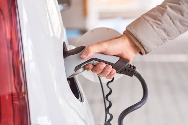 Kapanış görevlileri, kamu şarj istasyonunda elektrikli araba şarj eden el ele tutuşuyorlar. Çevre dostu ve sıfır emisyon aracı.