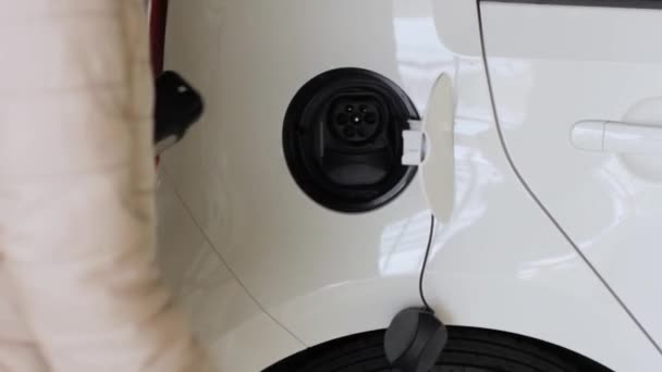O femeie apropiată vine la EV și deconectează un conector de încărcător în mașina electrică. Vehicul cu emisii zero — Videoclip de stoc