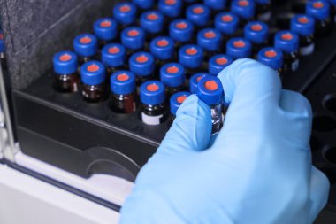 Kadın eli kapalı lastik eldiven ile cam bir şişe içine numune koyun mavi kapaklı HPLC sistemindeki otomatik ampler rafına. Ayrıştırma bileşikleri için yüksek performanslı sıvı kromatografi. Bilimsel