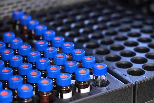 Γυάλινα φιαλίδια με μπλε πώματα βρίσκονται στο ράφι του συστήματος HPLC με αυτόματο δειγματολήπτη. Διαχωρισμός ενώσεων σε χημικό ή κλινικό εργαστήριο. Επιστημονικό και ερευνητικό έργο. Ανάπτυξη φαρμακευτικών προϊόντων. — Φωτογραφία Αρχείου