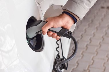 Elektrik kablosu kullanan ve EV şarj istasyonunda elektrikli araba şarjı yapan bir adam.. 