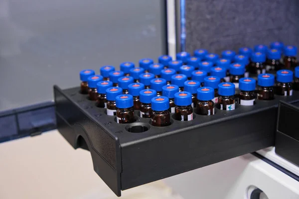 Glasflaschen mit blauen Kappen befinden sich im Rack des HPLC-Systems mit Autosampler. Trennung von Verbindungen in chemischen oder klinischen Labors. Wissenschaftliche und Forschungsarbeiten. Entwicklung von Arzneimitteln. — Stockfoto