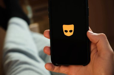 Erkek elinin altındaki akıllı telefondaki grindr uygulaması. Randevu ve buluşma için başvuru yapan bir adam. Sosyal ağ konsepti, Temmuz 2020, Prag, Çek Cumhuriyeti.