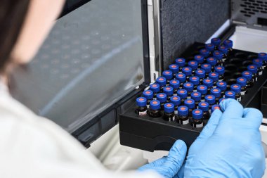 Beyaz önlüklü bir bilim adamı HPLC sisteminin otomatik amplifikatörüne numune yerleştiriyor. Kimya laboratuvarında yüksek performanslı sıvı kromatografi. İlaç veya aşının geliştirilmesi
