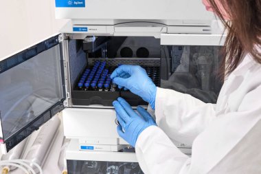 Beyaz önlüklü bir bilim adamı HPLC sisteminin otomatik amplifikatörüne numune yerleştiriyor. Kimya laboratuvarında yüksek performanslı sıvı kromatografi. İlaç veya aşının geliştirilmesi