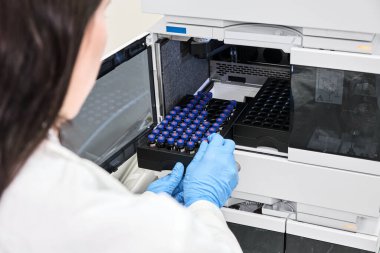 Beyaz önlüklü bir bilim adamı HPLC sisteminin otomatik amplifikatörüne numune yerleştiriyor. Kimya laboratuvarında yüksek performanslı sıvı kromatografi. İlaç veya aşının geliştirilmesi