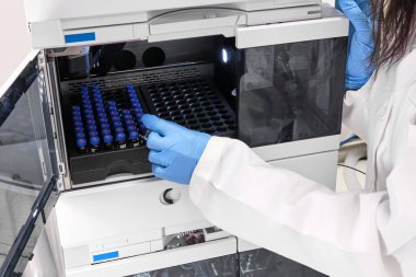 Beyaz önlüklü bir bilim adamı HPLC sisteminin otomatik amplifikatörüne numune yerleştiriyor. Kimya laboratuvarında yüksek performanslı sıvı kromatografi. İlaç veya aşının geliştirilmesi