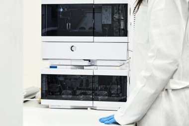 Lastik eldivenli ve beyaz önlüklü bilim adamı organik bileşikleri ayırmak için yüksek performanslı sıvı kromatografi HPLC 'nin yanında duruyor. Analitik kimya laboratuvarı. İşlem analiz ediliyor.