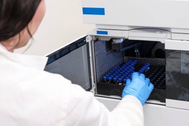 Beyaz önlüklü bir bilim adamı HPLC sisteminin otomatik amplifikatörüne numune yerleştiriyor. Kimya laboratuvarında yüksek performanslı sıvı kromatografi. İlaç veya aşının geliştirilmesi