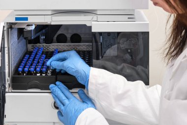 Beyaz önlüklü bir bilim adamı HPLC sisteminin otomatik amplifikatörüne numune yerleştiriyor. Kimya laboratuvarında yüksek performanslı sıvı kromatografi. İlaç veya aşının geliştirilmesi