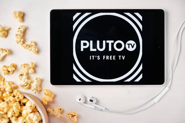 Pluto TV auf dem Bildschirm des Tablets mit Popcorn-Box und Apple-Kopfhörern im Hintergrund. Werbung oder Nachrichteninhalte, August 2020, San Francisco, USA — Stockfoto