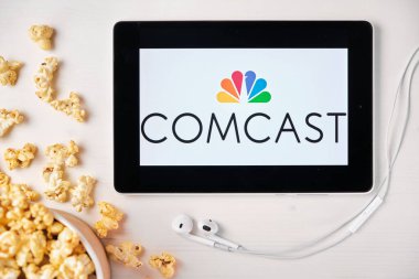 Comcast on the screen of the tablet with popcorn box and Apple earphones on the background. Advertising or news content, August 2020, San Francisco, USA clipart