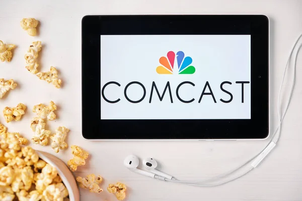 Comcast sullo schermo del tablet con scatola di popcorn e auricolari Apple sullo sfondo. Pubblicità o contenuti di notizie, agosto 2020, San Francisco, Stati Uniti — Foto Stock