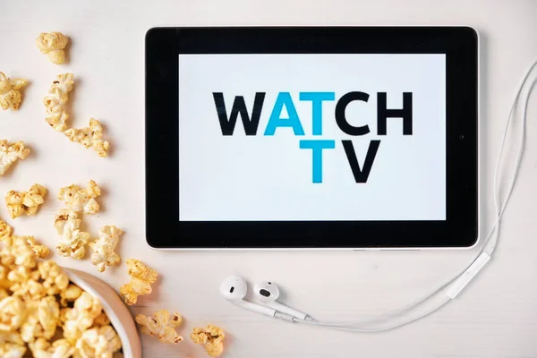 Fernsehen auf dem Bildschirm des Tablets mit Popcorn-Box und Apple-Kopfhörern im Hintergrund. Werbung oder Nachrichteninhalte, August 2020, San Francisco, USA — Stockfoto