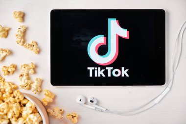 Tabletin ekranında TikToK logosu ve arkasında patlamış mısır kutusu ve Apple kulaklıkları var. Arkadaşlarla paylaşılacak eğlenceli videolar oluşturma uygulaması Reklamcılık veya haber içeriği, Ağustos 2020, San