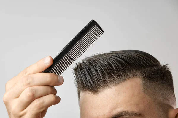 Fechar jovem penteando o cabelo com um pente de plástico. Cabelo de estilo após barbearia. — Fotografia de Stock