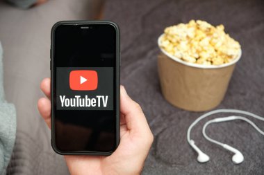 Yanında Apple kulaklıkları ve patlamış mısır kutusu olan YouTube TV logosunun olduğu cep telefonunu kapatan adamlar, Bedava TV konsepti, Ağustos 2020, San Francisco, ABD