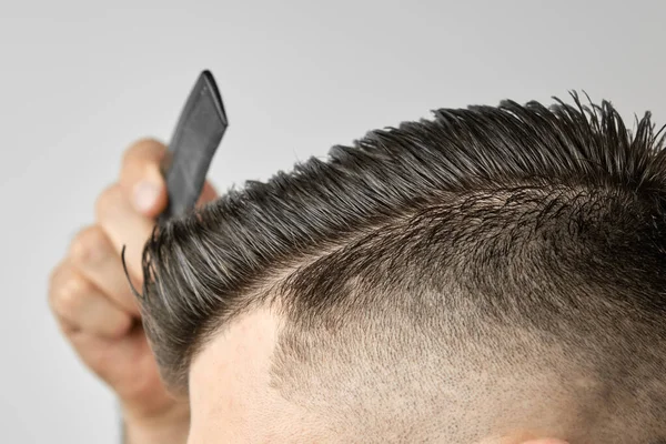 Großaufnahme junger Mann kämmt seine Haare mit einem Plastikkamm. Haare stylen nach dem Friseur. — Stockfoto