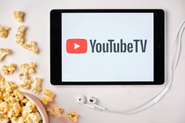 Tabletin ekranındaki Youtube TV logosu beyaz masaya serpilmiş ve üzerine patlamış mısır serpiştirilmiş. Tabletin yanındaki Apple kulaklıklar Youtube uygulamasını gösteriyor, Ağustos 2020, San Francisco, ABD