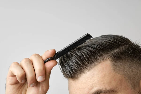 Close up young man combing his hair with a plastic comb. Styling hair after barbershop. Cosmetology treatment against dandruff on hair concept. — Stock Photo, Image
