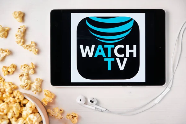 Sehen Sie das TV-Logo auf dem Bildschirm des Tablets, das auf dem weißen Tisch liegt und mit Popcorn bestreut ist. Apple-Kopfhörer neben dem Tablet mit einer Watch-TV-App, August 2020, San Francisco, USA — Stockfoto