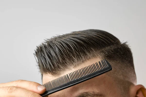 Großaufnahme junger Mann kämmt seine Haare mit einem Plastikkamm. Haare stylen nach dem Friseur. — Stockfoto