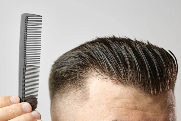 Zblízka si mladý muž česá vlasy plastovým hřebenem. Styling vlasy po holičství. — Stock fotografie