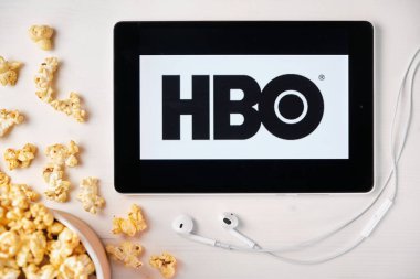 Beyaz masada duran tabletin ekranında HBO logosu ve üzerine patlamış mısır serpiştirilmiş. Tabletin yanındaki Apple kulaklıklar HBO uygulamasını gösteriyor, Ağustos 2020, San Francisco, ABD