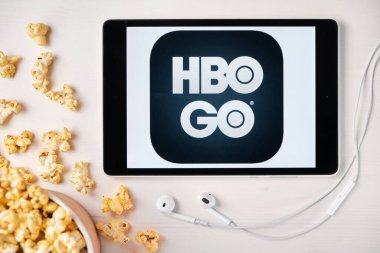 Beyaz masada duran tabletin ekranında HBO GO logosu ve üzerine patlamış mısır serpiştirilmiş. Tabletin yanındaki Apple kulaklıklar HBO uygulamasını gösteriyor, Ağustos 2020, San Francisco, ABD
