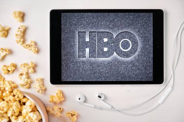 Beyaz masada duran tabletin ekranında HBO logosu ve üzerine patlamış mısır serpiştirilmiş. Tabletin yanındaki Apple kulaklıklar HBO uygulamasını gösteriyor, Ağustos 2020, San Francisco, ABD