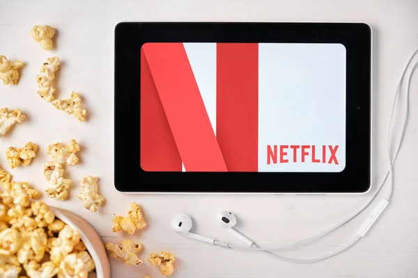 Das Netflix-Logo auf dem Bildschirm des Tablets liegt auf dem weißen Tisch und bestreut es mit Popcorn. Apple-Kopfhörer neben dem Tablet mit einer Netflix-App, August 2020, San Francisco, USA — Stockfoto