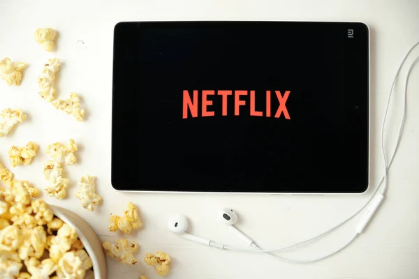 Das Netflix-Logo auf dem Bildschirm des Tablets liegt auf dem weißen Tisch und bestreut es mit Popcorn. Apple-Kopfhörer neben dem Tablet mit einer Netflix-App, August 2020, San Francisco, USA — Stockfoto
