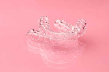 Pembe arka planda iki tane görünmez diş izi var. Hizalandıktan sonra diş düzeltmek için ortodontik geçici diş telleri çıkarılabilir. Parantez üstüne terapi. 