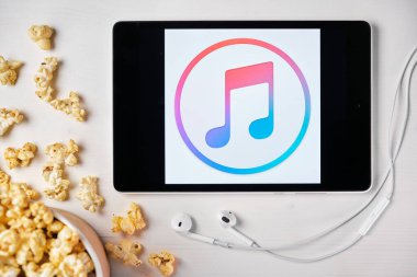 Elma müzik logosu beyaz masada duran tabletin ekranında ve üzerine patlamış mısır serpiştirilmiş. Tabletin yanındaki Apple kulaklıklar, Ağustos 2020, San Francisco, ABD