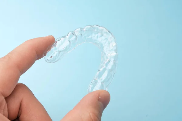 In Großaufnahme hält man eine transparente abnehmbare Zahnspange zur Zahnaufhellung auf blauem Hintergrund mit Kopierraum. Unsichtbare Zahnausrichtungen für Glättungszähne. — Stockfoto